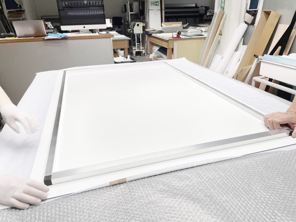 Ein kaschierter Fine-Art-Print wird im Labor mit Handschuhen aus der Schutzfolie gehoben